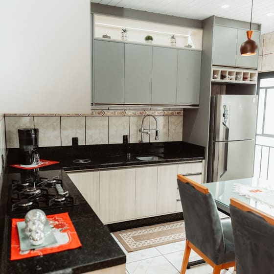Cozinha planejada em L com armários aéreos verde-acinzentados e bancada de granito preto